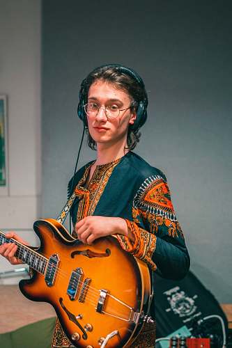 human man in blue and orange long sleeve shirt playing brown electric guitar person